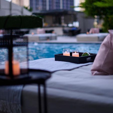 Jw Marriott Kuala Lumpur Hotel Exterior photo The photo depicts a serene setting by a pool. In the foreground, there is a table with a lantern and candles, creating a cozy atmosphere. A tray on a lounge area holds three glasses and some greenery. Soft pillows add comfort, and the pool reflects t