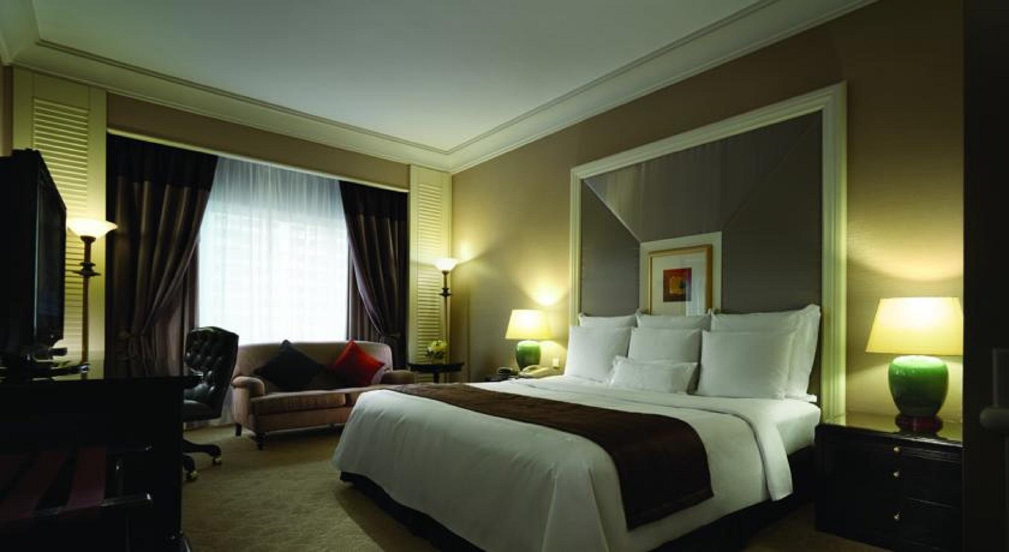 Jw Marriott Kuala Lumpur Hotel Exterior photo The photo shows a well-furnished hotel bedroom. It features a large bed with white bedding and brown accents. There are two bedside lamps providing soft lighting. To the side, there's a comfortable-looking sofa with decorative pillows and a desk with