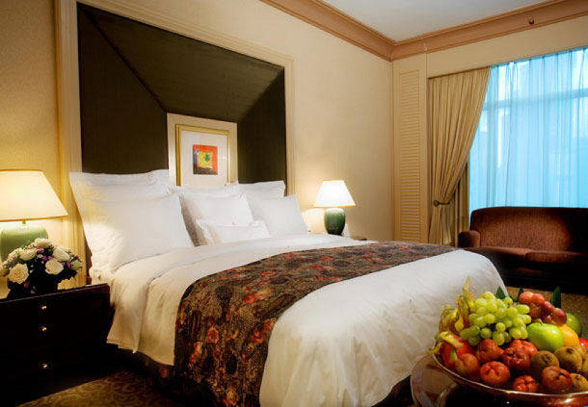 Jw Marriott Kuala Lumpur Hotel Room photo The photo shows a well-decorated hotel room. In the center, there is a large bed with white bedding and a decorative throw blanket featuring floral patterns. On either side of the bed, there are bedside tables with lamps. A comfortable armchair is po