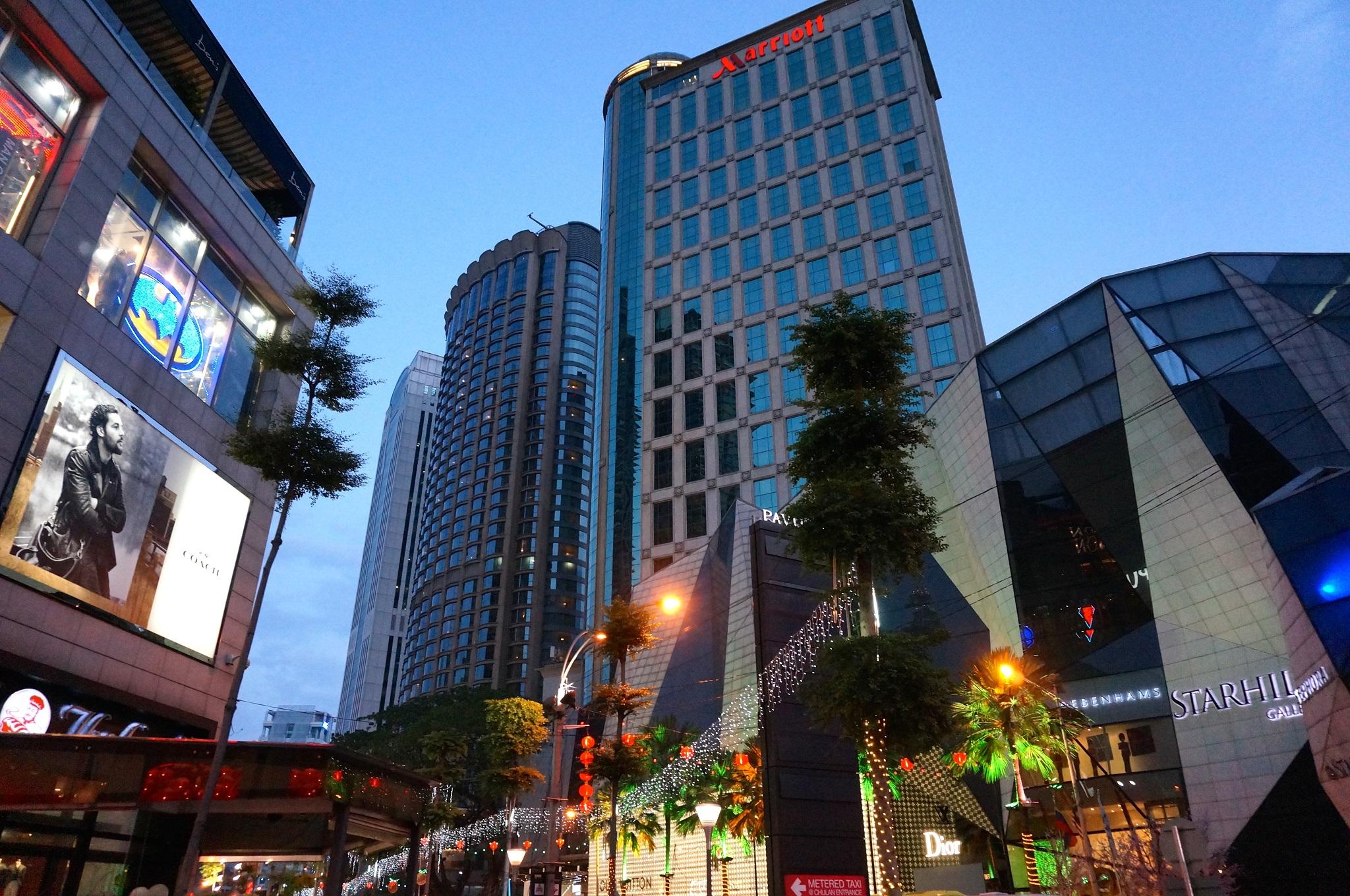 Jw Marriott Kuala Lumpur Hotel Exterior photo The photo shows a modern urban scene during twilight. There are several tall buildings, including a notable high-rise with a glass facade, suggesting a commercial area. The architecture appears contemporary, with a mix of reflective surfaces and illu
