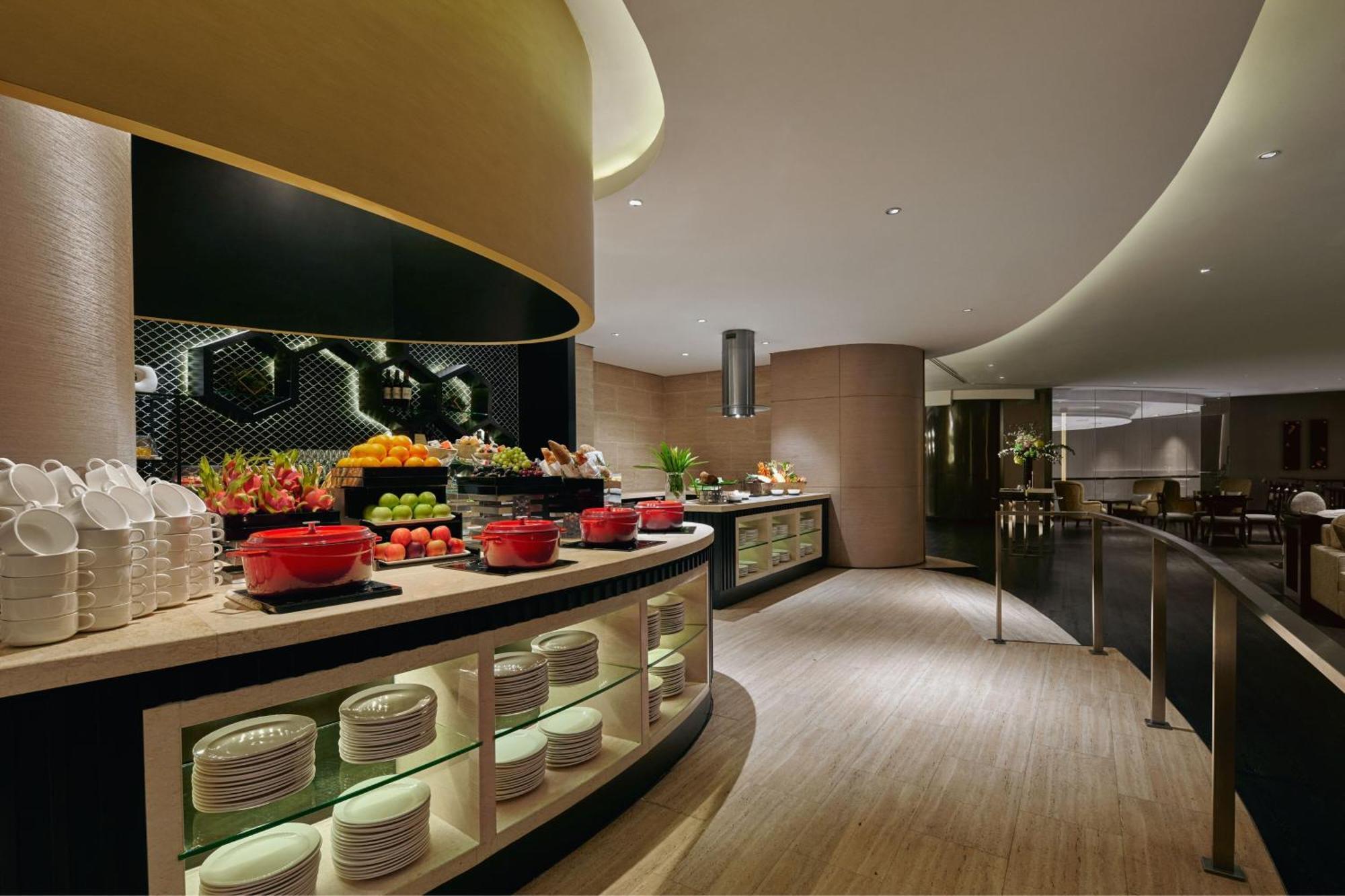 Jw Marriott Kuala Lumpur Hotel Exterior photo The photo shows a stylish buffet area in a modern restaurant or hotel. There is a curved counter featuring a variety of food options, including fresh fruits and red bowls filled with dishes. Behind the counter, there are neatly arranged plates and a 