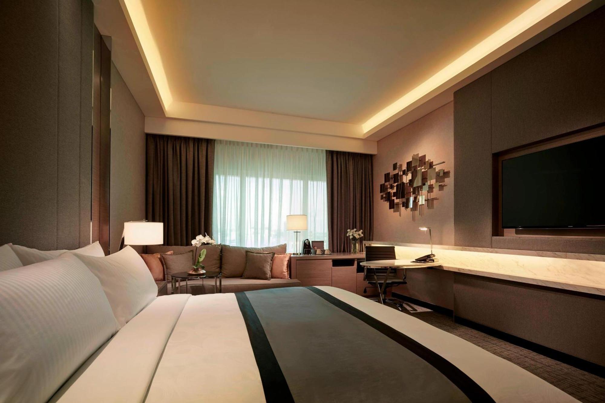 Jw Marriott Kuala Lumpur Hotel Exterior photo The photo shows a modern hotel room with a sophisticated design. It features a large bed with crisp white linens and a decorative gray and black throw blanket. There are two bedside lamps providing soft lighting. In the background, there is a seating