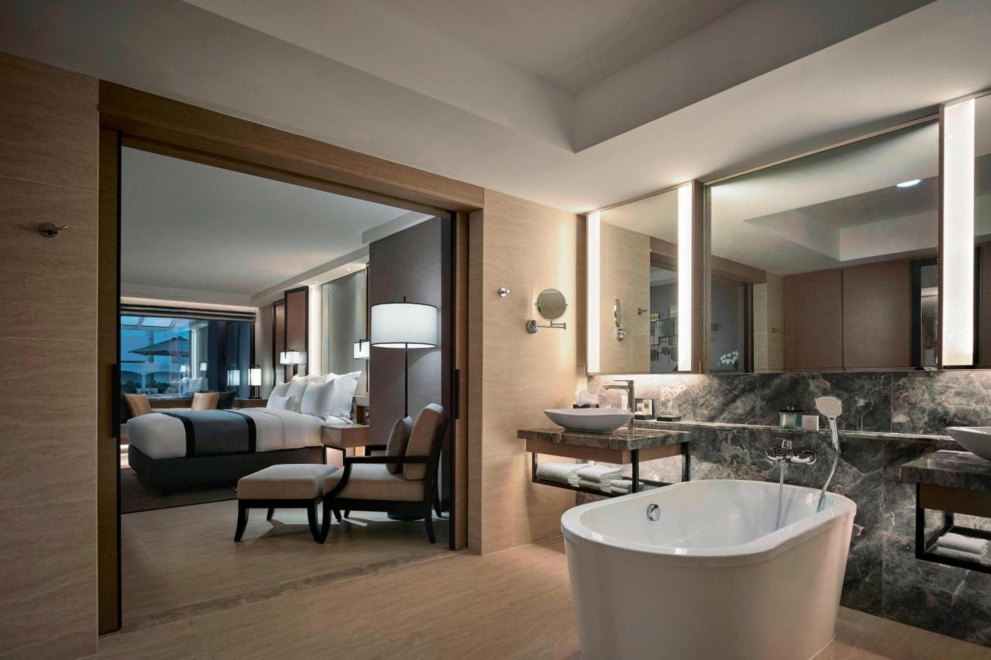 Jw Marriott Kuala Lumpur Hotel Exterior photo The photo shows a luxurious hotel suite. In the foreground, there is a freestanding bathtub situated on a wooden floor. The bathroom area features modern fixtures, including a sink and a countertop made of dark stone. 

Through an open doorway, a wel