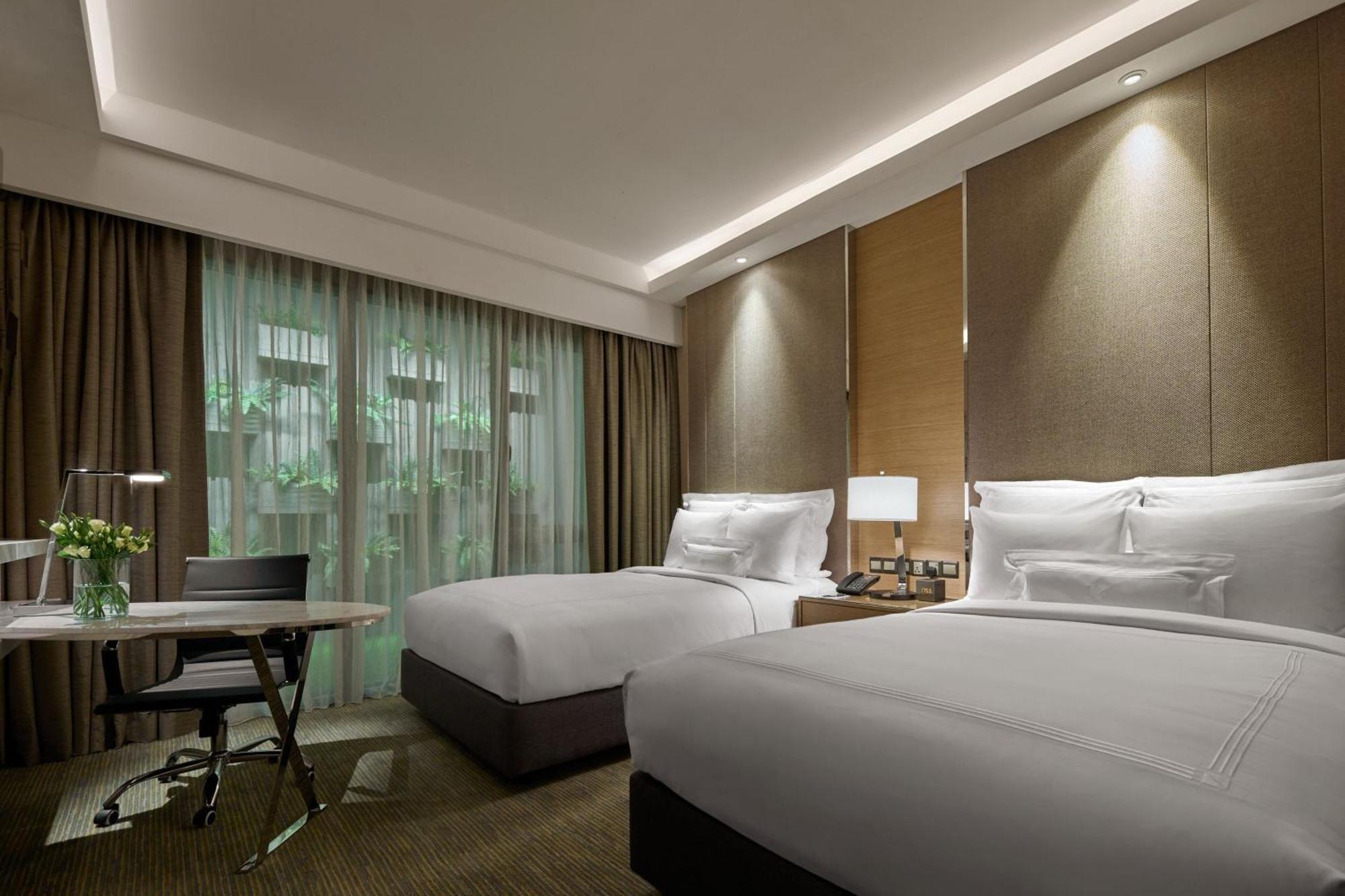 Jw Marriott Kuala Lumpur Hotel Exterior photo The photo shows a modern hotel room featuring two beds with white bedding. The walls are styled with a combination of textured panels and soft lighting. There's a large window draped with sheer curtains, allowing natural light to enter the room. A sm