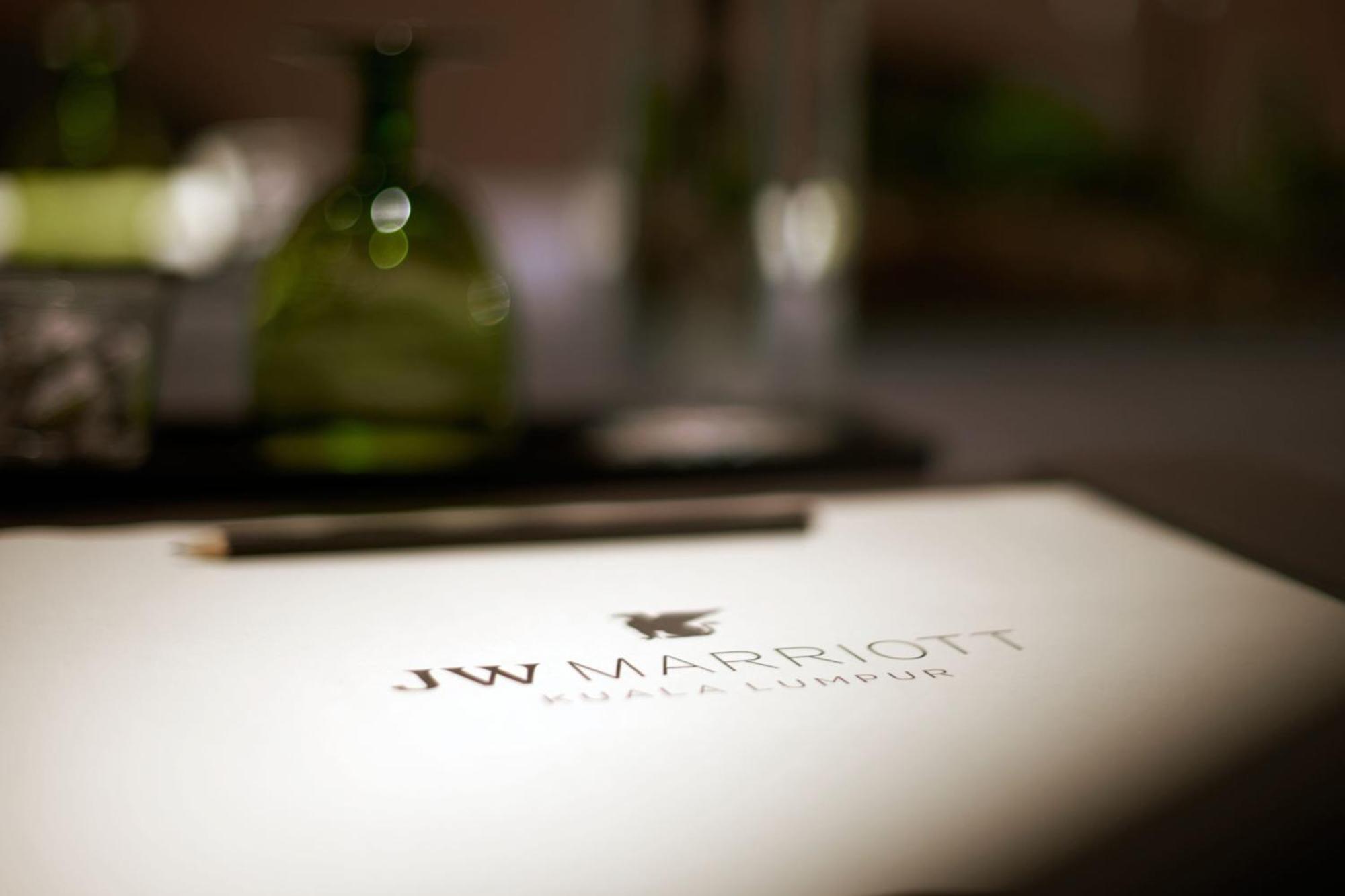 Jw Marriott Kuala Lumpur Hotel Exterior photo The photo shows a close-up of a table setting with a focus on a menu or notepad featuring the logo of "JW Marriott Kuala Lumpur." The logo is prominently displayed in a refined, elegant font. In the background, there are green decorative bottles and 