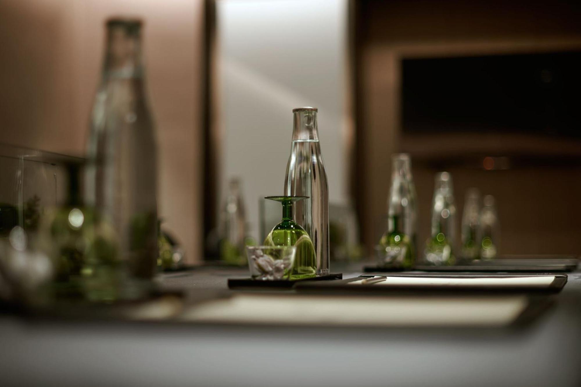 Jw Marriott Kuala Lumpur Hotel Exterior photo The photo shows a neatly arranged table setting, likely in a conference or dining room. It features several glass water bottles of various sizes, some of which are filled with water. In the center, there is a smaller glass container, possibly for hol