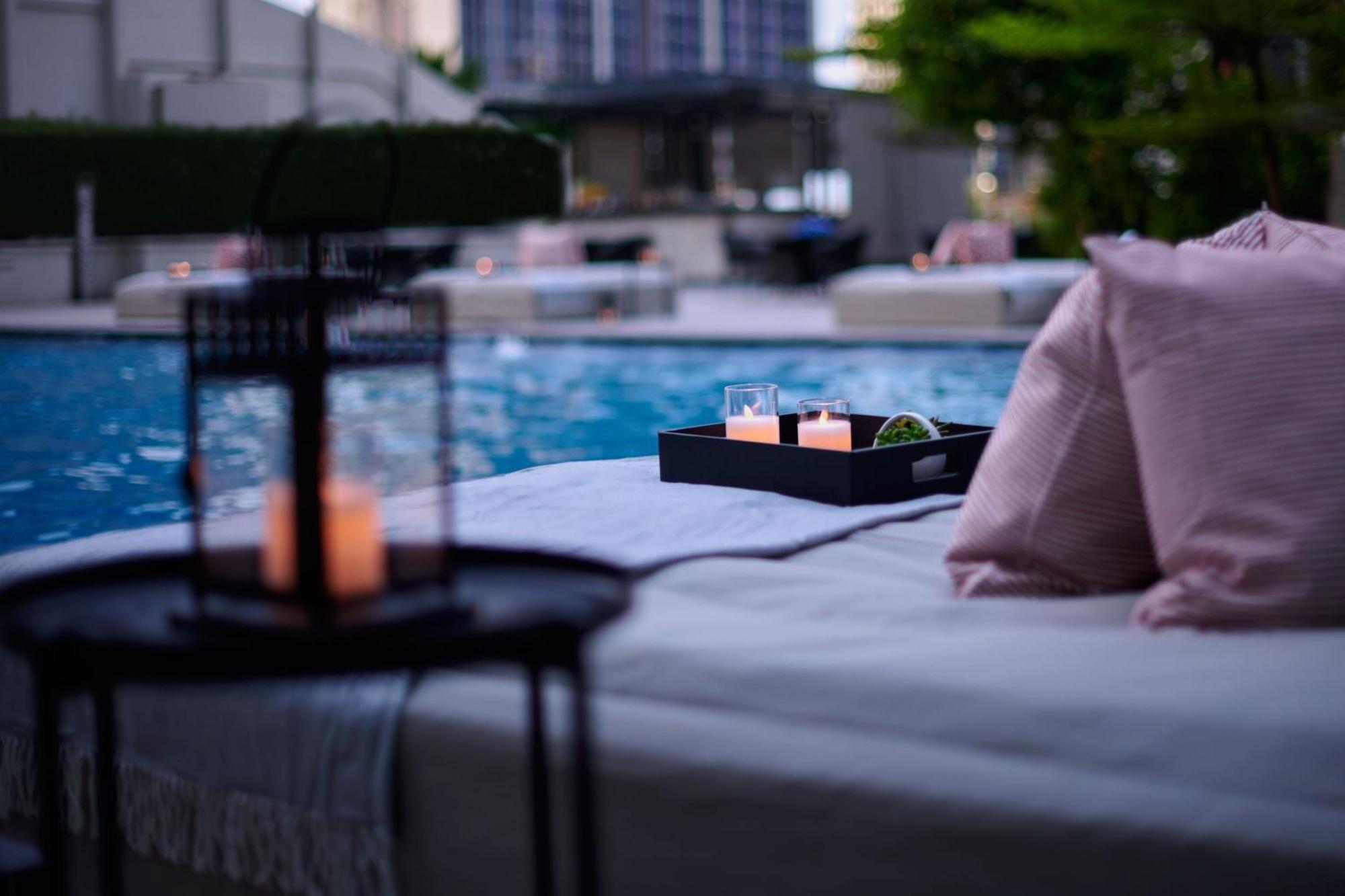 Jw Marriott Kuala Lumpur Hotel Exterior photo The photo depicts a serene setting by a pool. In the foreground, there is a table with a lantern and candles, creating a cozy atmosphere. A tray on a lounge area holds three glasses and some greenery. Soft pillows add comfort, and the pool reflects t