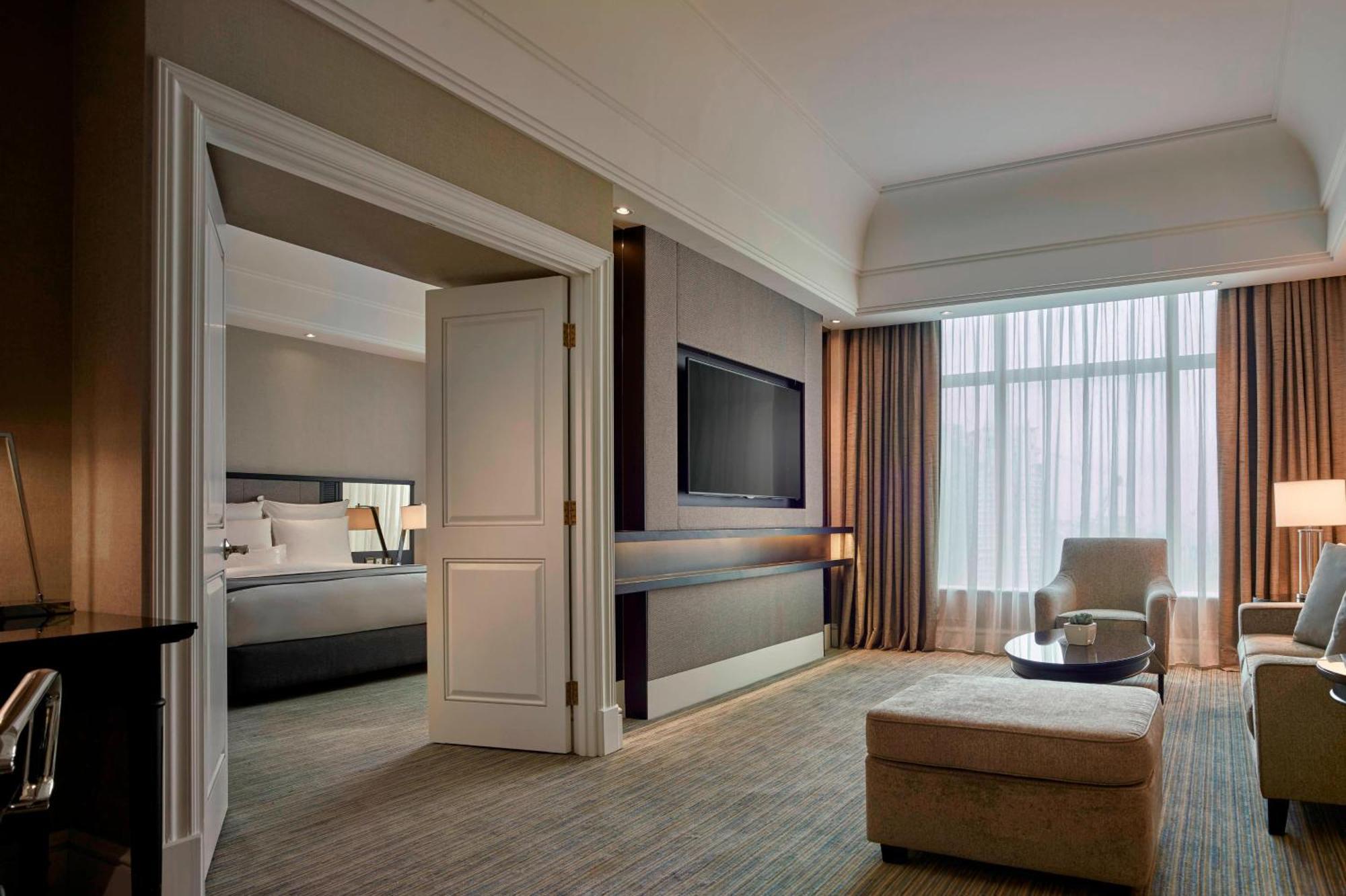 Jw Marriott Kuala Lumpur Hotel Exterior photo The photo shows a modern hotel room designed with a neutral color palette. There is a spacious living area featuring a comfortable chair and a coffee table, along with a plush ottoman. In the background, a large window lets in natural light, covered 