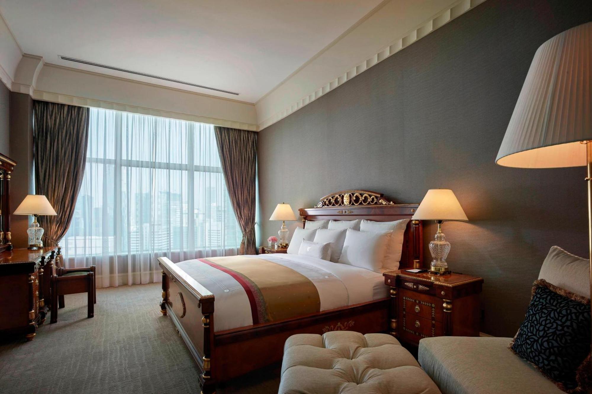 Jw Marriott Kuala Lumpur Hotel Exterior photo The image shows an elegant hotel bedroom. The room features a large bed with a richly designed headboard and a comfortable bedding ensemble. There are two bedside tables, each with a lamp, providing soft lighting. A plush ottoman is located at the fo