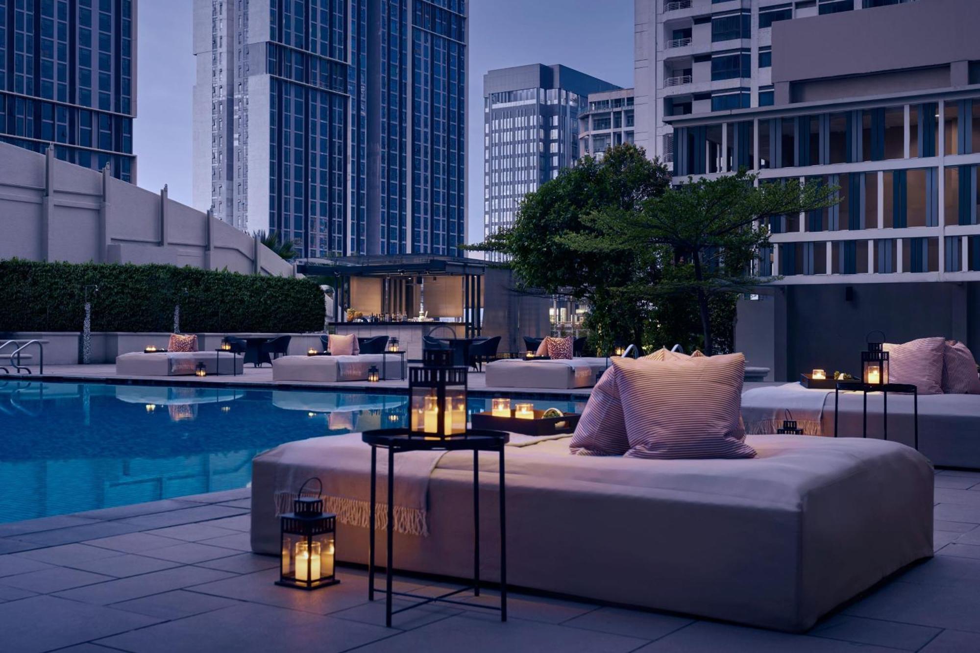 Jw Marriott Kuala Lumpur Hotel Exterior photo The photo depicts a stylish outdoor area featuring a swimming pool. Surrounding the pool are lounge beds adorned with soft pillows, creating a relaxed atmosphere. Several small tables with lanterns are strategically placed, adding to the ambiance, pa