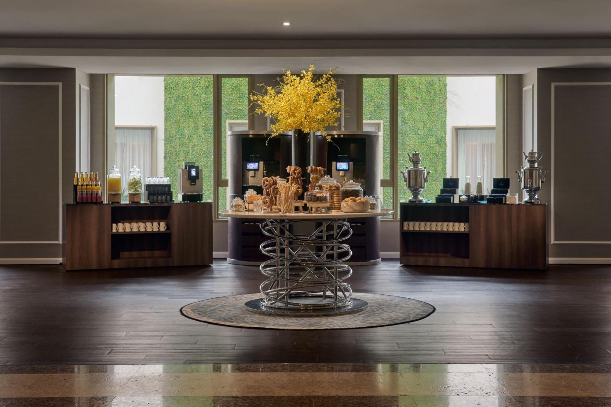 Jw Marriott Kuala Lumpur Hotel Exterior photo The photo shows a modern, elegant indoor space that appears to be a hospitality area, possibly a hotel lobby or lounge. At the center, there is a round table featuring an attractive display of baked goods and pastries. Surrounding this table are wood