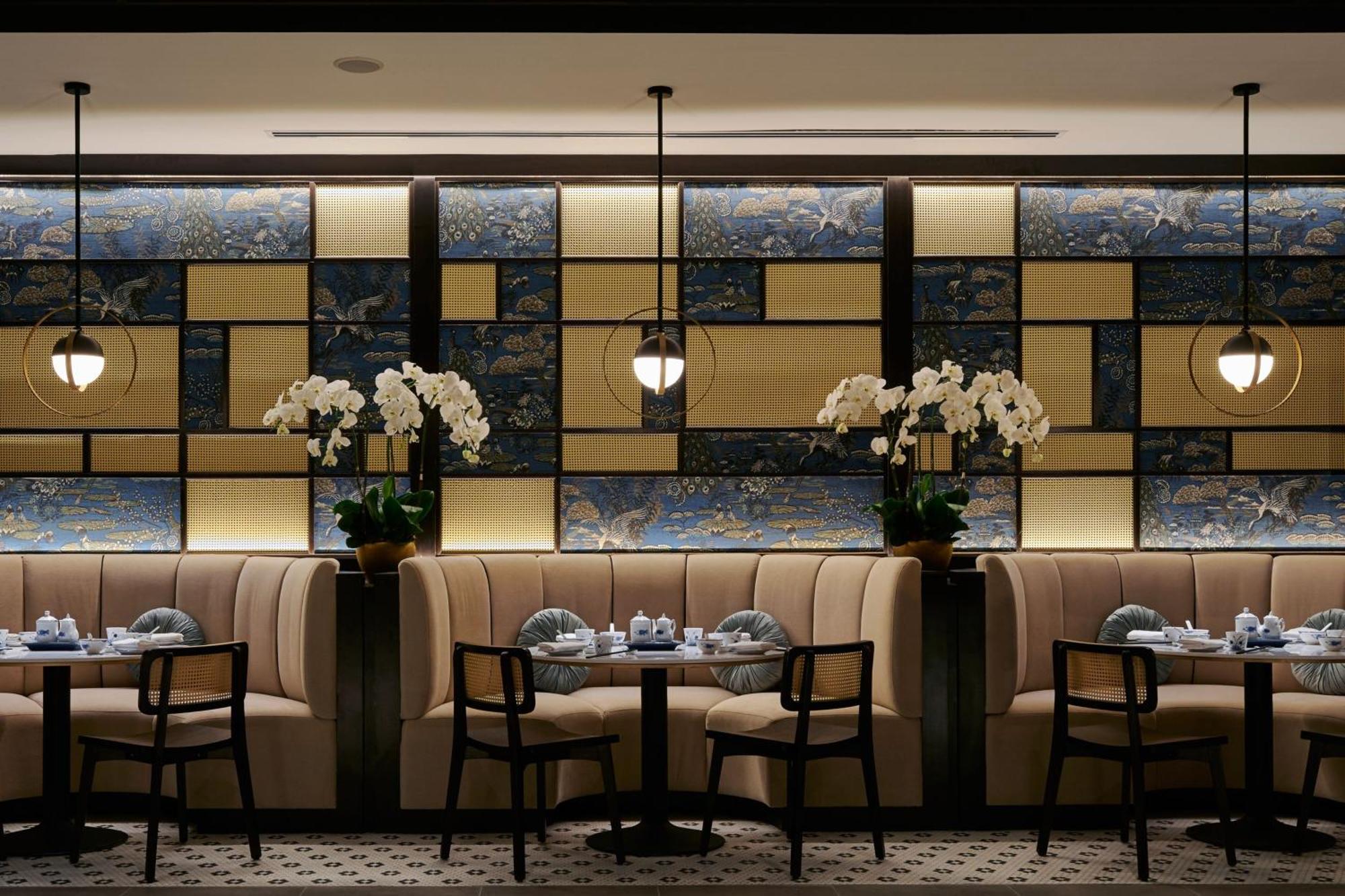 Jw Marriott Kuala Lumpur Hotel Exterior photo The photo shows an elegant restaurant interior. The design features a stylish, modern aesthetic with tufted beige banquettes along the walls and dark wooden chairs. There are small round tables set with dishes and blue-and-white tableware. The backdr