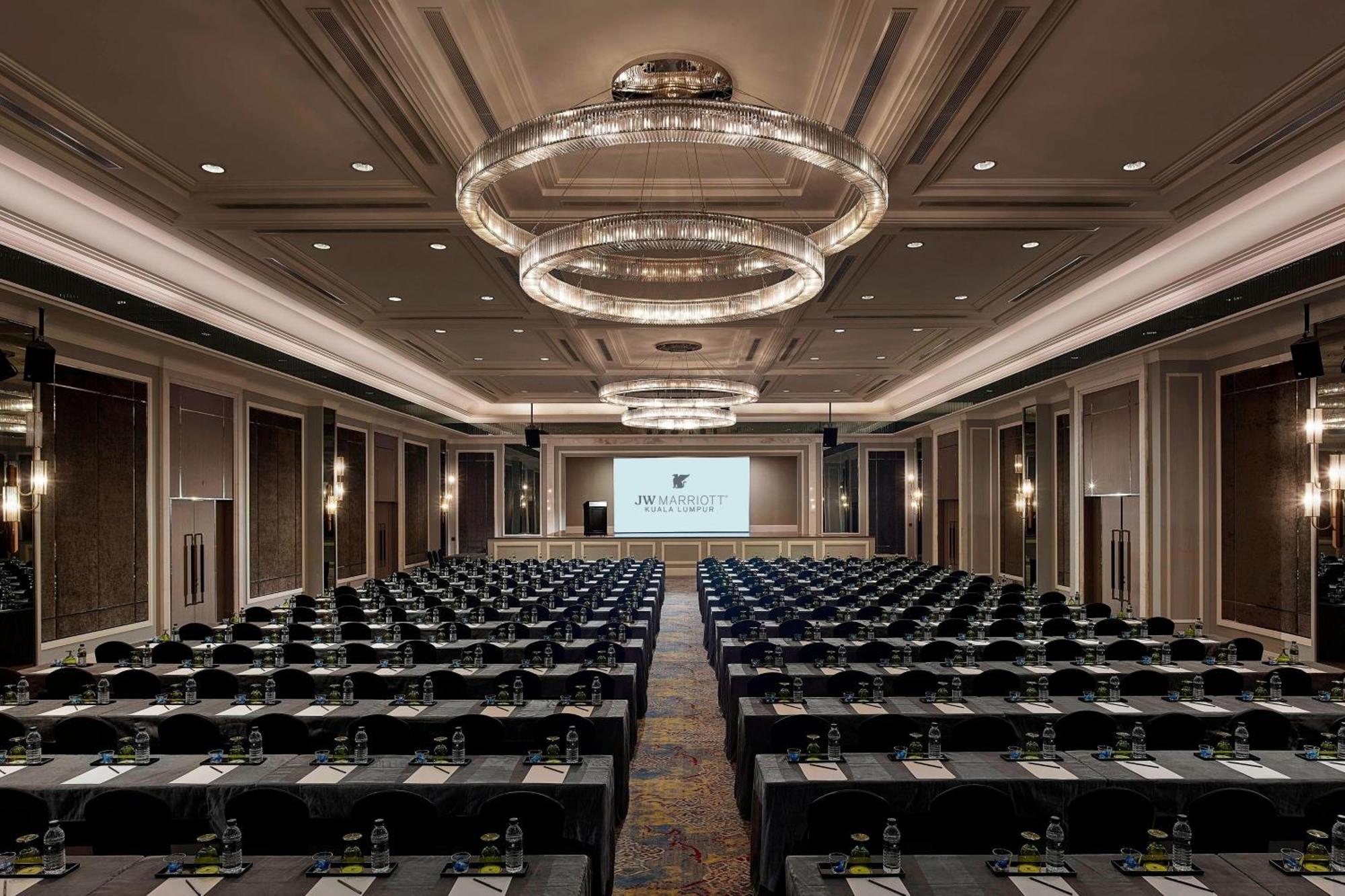 Jw Marriott Kuala Lumpur Hotel Exterior photo The photo shows a large conference room set up for a meeting or event. There are numerous rows of tables arranged in a classroom or theater style, with chairs facing the front where a large screen is set up, likely for presentations. The room has ele