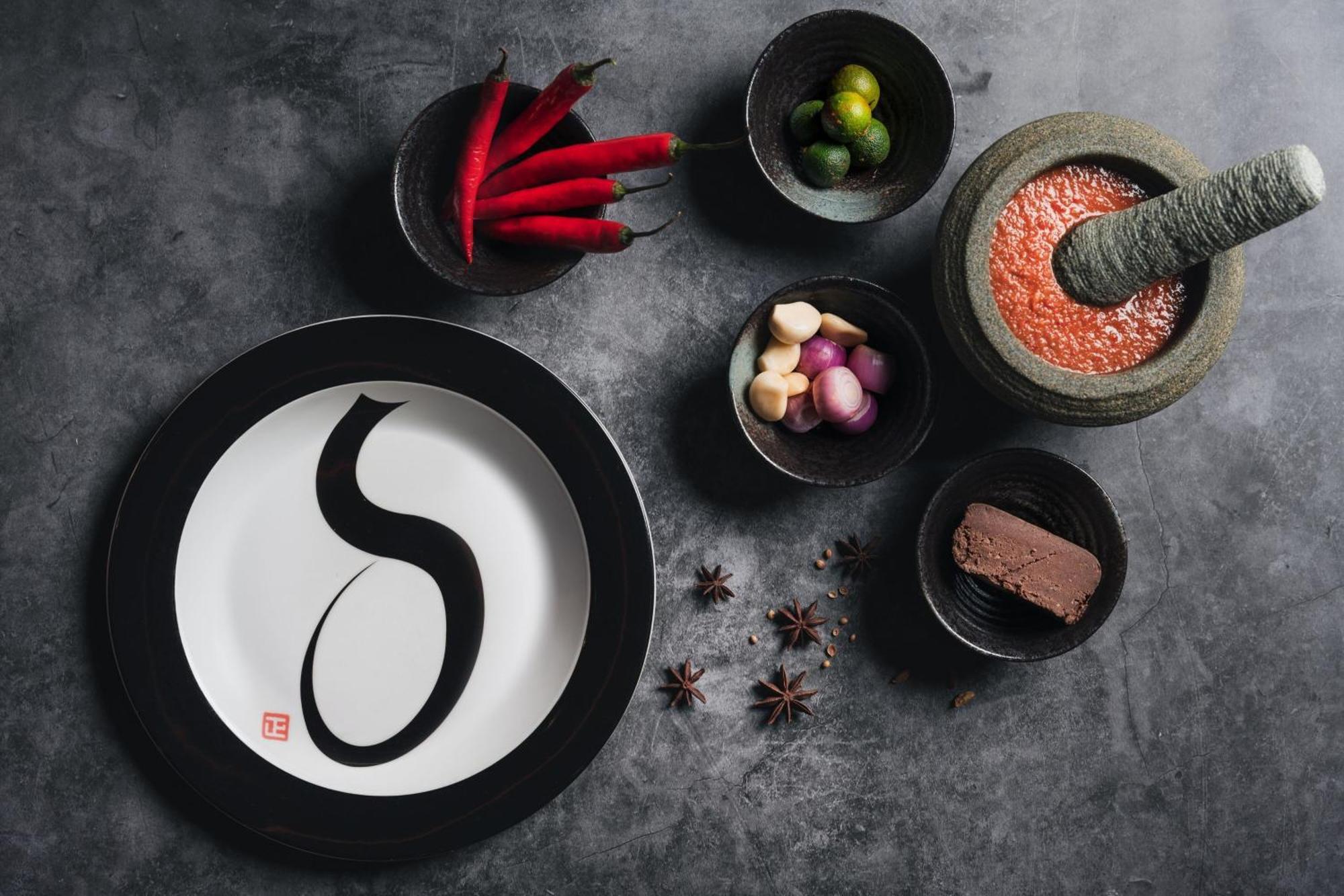 Jw Marriott Kuala Lumpur Hotel Exterior photo The photo depicts an artistic arrangement of food items on a textured gray surface. In the center, there is a white plate with a black rim featuring a stylized black letter or character. Surrounding the plate are several small bowls filled with vario
