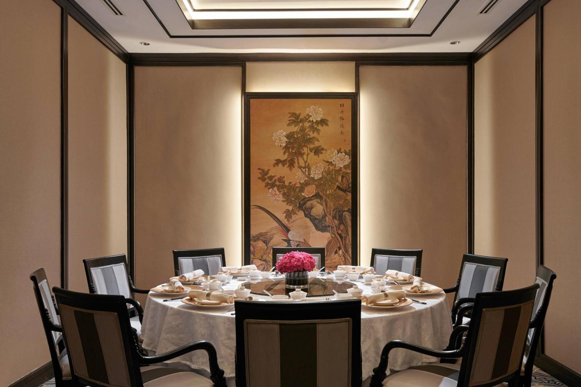 Jw Marriott Kuala Lumpur Hotel Exterior photo The photo shows an elegant dining room setup featuring a round table covered with a white tablecloth. The table is arranged with several place settings, including plates, cups, and a decorative centerpiece with flowers. The walls are adorned with a t